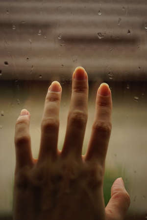 Hand touches a window in rain drops.の写真素材