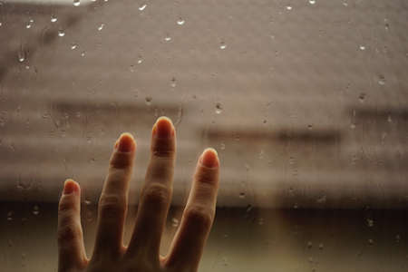 Hand touches a window with rain drops. Roof background in blur.の写真素材