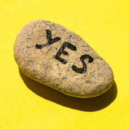 Pebble stone with the text yes on yellow table.の写真素材