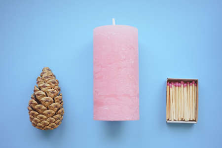 Matches in open box, pale pink candle and pine cone on the blue tableの写真素材