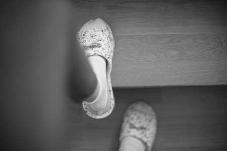 Female feet in socks and slippers are walking up the stairs. Black and white photoの写真素材