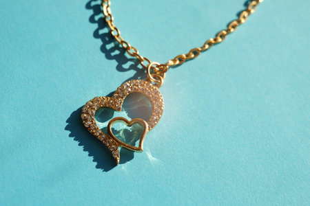 Gold chain with a pendant in the form of two hearts on a sunny blue table.の写真素材