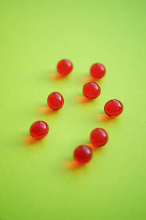 Round red vitamins on a vivid green table.