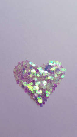 Purple heart made of sequins on a lilac table.
