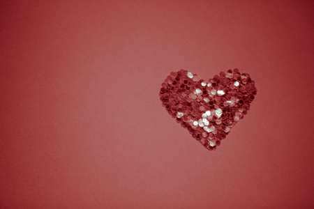 Neat heart made of sequins on a red table. Copy space