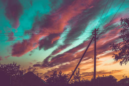 Silhouettes of an electric pole, a house and trees against a blue sunset sky with red clouds.の写真素材