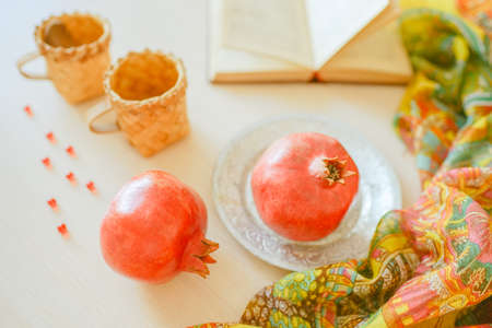 Whole pomegranates in plate, opened cookbook, vitamins and cups on the table.の写真素材