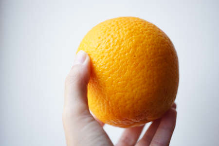 Ripe orange in female fingers on white background