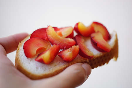 Sandwich with pieces of plum fruit in a female hand on a white background.の写真素材