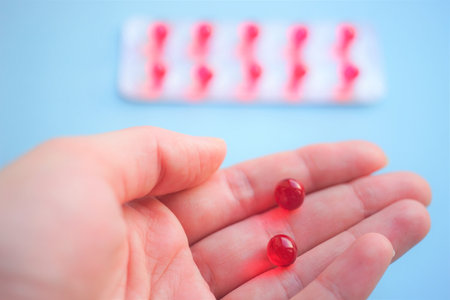 Round red vitamins in human palm on pale blue background.