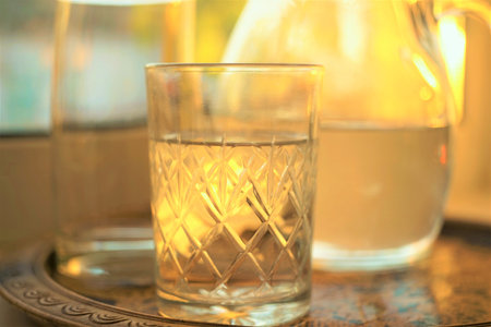 Glass of water and jug of water in a tray on the sunny windowsill.の写真素材