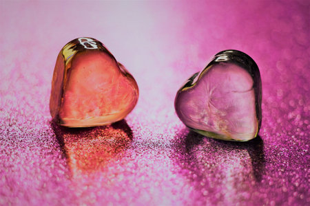 Amber and pink glass hearts on glitter purple table.の写真素材