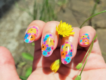 Female hand with beautiful floral manicure. Yellow flower in female hand in sunny garden.の写真素材