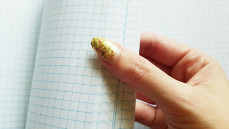 Female hand with a golden manicure flips through a blank checkered notebookの写真素材