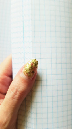 Young female hand with a golden manicure flips through a blank checkered notebook.の写真素材