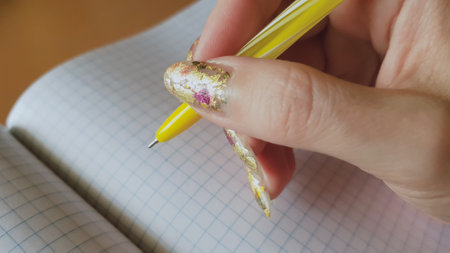 A beautiful female hand with a golden manicure is preparing to write in a blank checkered notebook