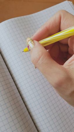 A beautiful female hand with a golden manicure is preparing to write in a blank checkered notebookの写真素材