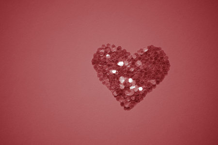Neat heart made of sequins on a red table. Copy spaceの写真素材