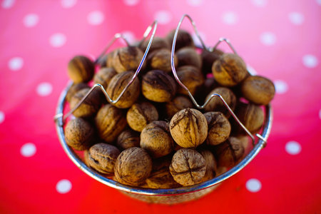 A bowl full of walnuts on a red tablecloth with white dots.