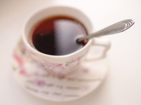 Spoon in a cup of drink. Cup of tea on a saucer in blur on a white tableの写真素材