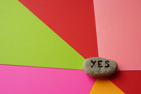 Pebble stone with text yes on them. Colorful background from sheets of paper.の写真素材