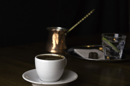 a glass of coffee with coffee pot and chocolate beside a coffee with milk in a white cup placed on a brown tableの写真素材