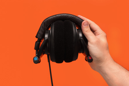 DJ headphones in hand. Front view. On orange background