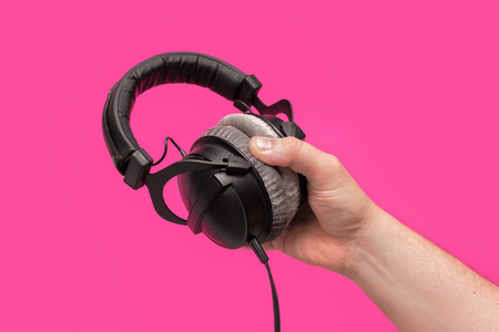 Dark headphones in hand. On pink backgroundの写真素材
