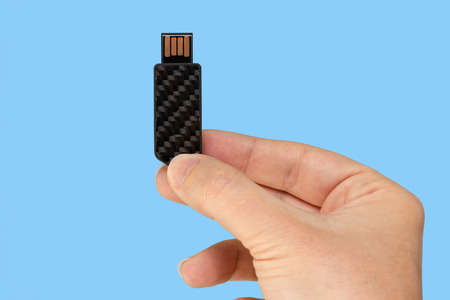 Black USB memory stick in hand. Blue backgroundの写真素材