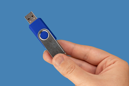 Blue USB memory stick on hand with blue background. Front view