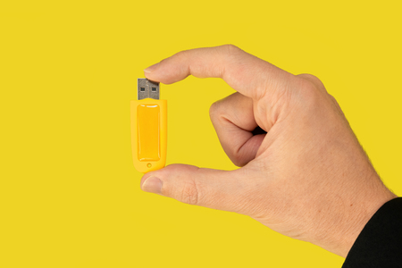 Yellow USB pen drive on hand with isolated yellow background. Front view