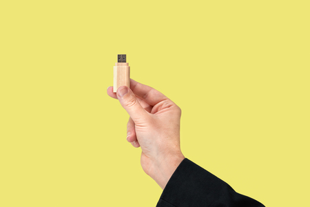 Wood USB Flash drive on hand with isolated yellow background. Front view