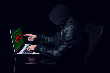 Anonymous hacker pointing the screen. Seen from the side