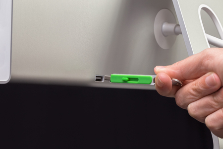USB Green flash memory connected by hand to a monitor. Dark background