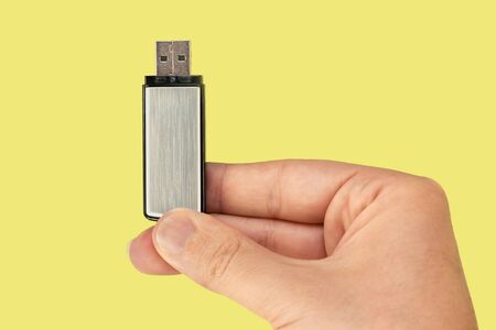 Metal flash drive on hand with isolated yellow background. Front viewの写真素材