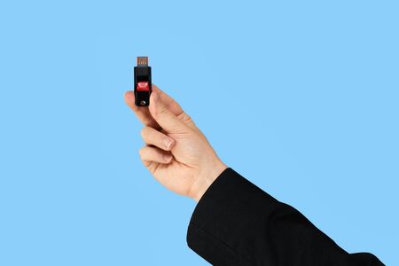 Black memory stick on hand with blue background. Front viewの写真素材