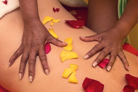 An African-American woman gives a relaxing massage to a Caucasian man. Environment full of rose petalsの写真素材