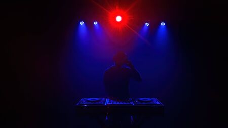 DJ - Silhouette of the Disc jockey playing with the mixing desk. Lights and laser of discothequeの写真素材