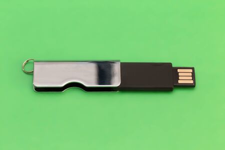 Rectangular metallic USB flash drive on a green background. Close-up