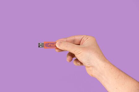 Orange USB flash memory on hand with isolated violet background. Front viewの写真素材