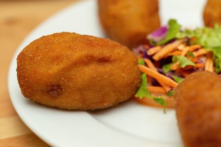 Close-up of a croquette with salad on a plate. Macro with very unfocused backgroundの写真素材