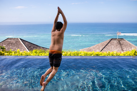 Boy jumps into swimming pool with beautiful blue ocean background in sunshine day