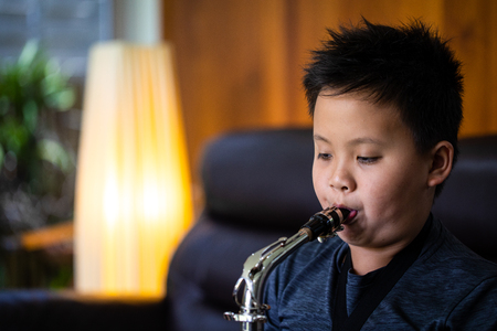 Asian boy blow saxophone in living room, headshot photographyの写真素材