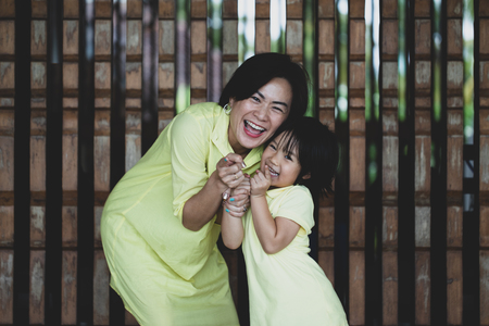 playful mother and duagther with yellow clothes hold hand together and smileの写真素材