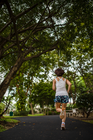 Rear view of Asian woman speed running in the park with greenery environmentの写真素材