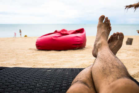 feet on beachchair at beachfront with red beanbag backgroundの写真素材