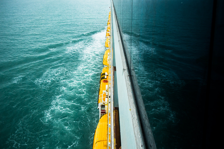 Yellow lifeboats  from upper side view of cruise ship and splashing wave in oceanの写真素材