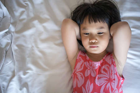 Chilled out Asian adorable child on white bedの写真素材