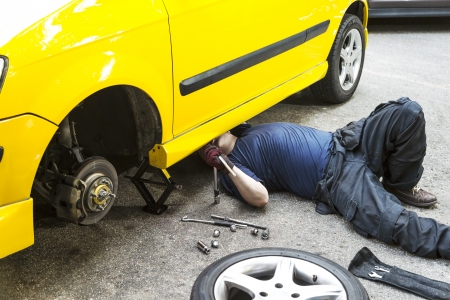 A mechanic underneath a yellow car doing maintain job.の写真素材
