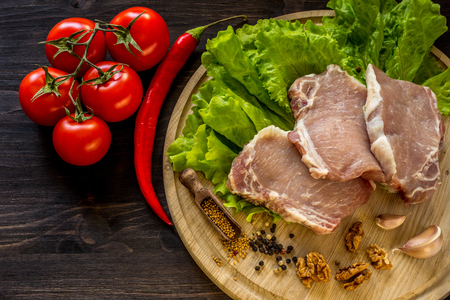 Slices of raw meat. Pork escalope on a wooden board. With the ingredients for cooking.の写真素材